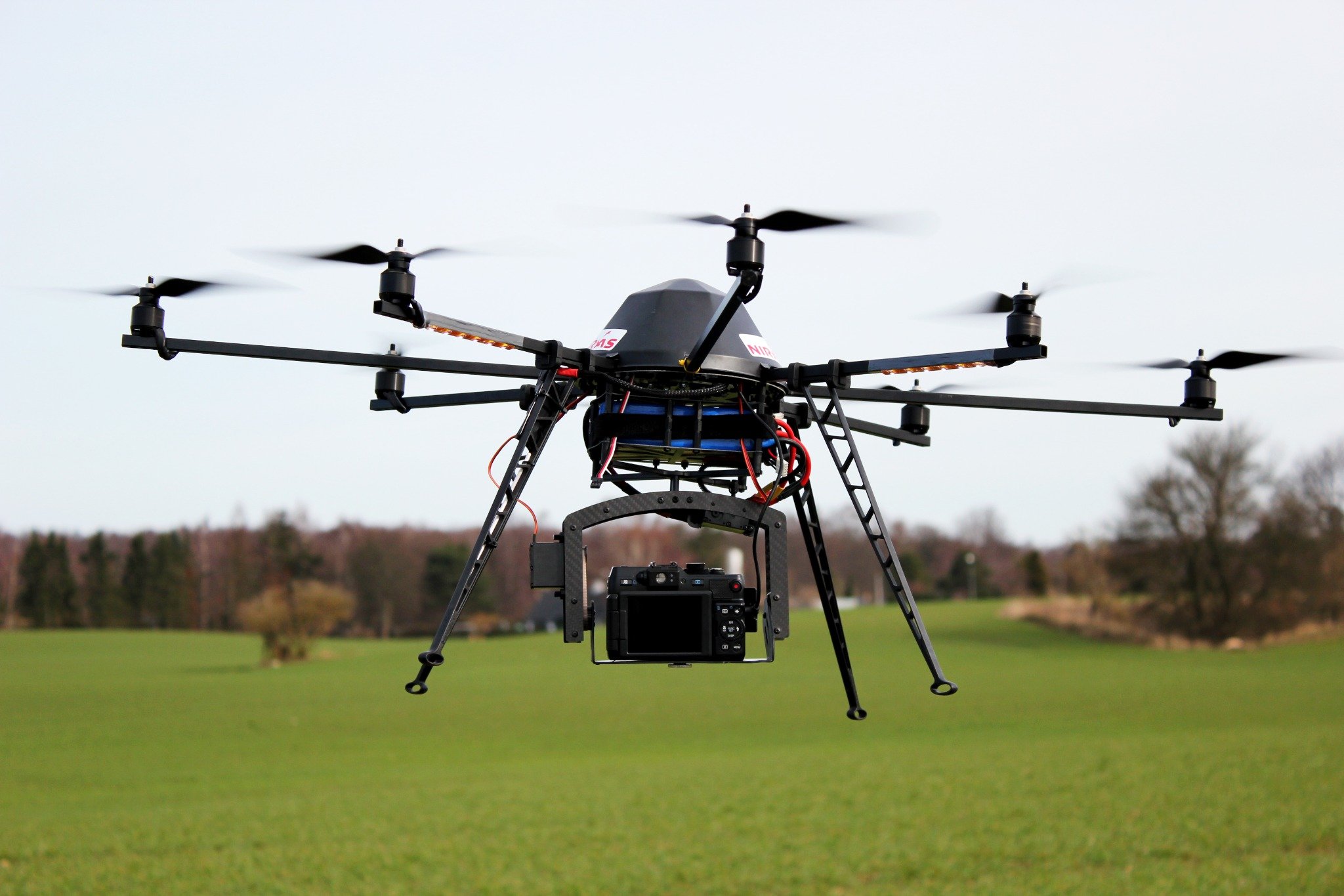 Drone with camera flying low over a grassy field with trees in the background